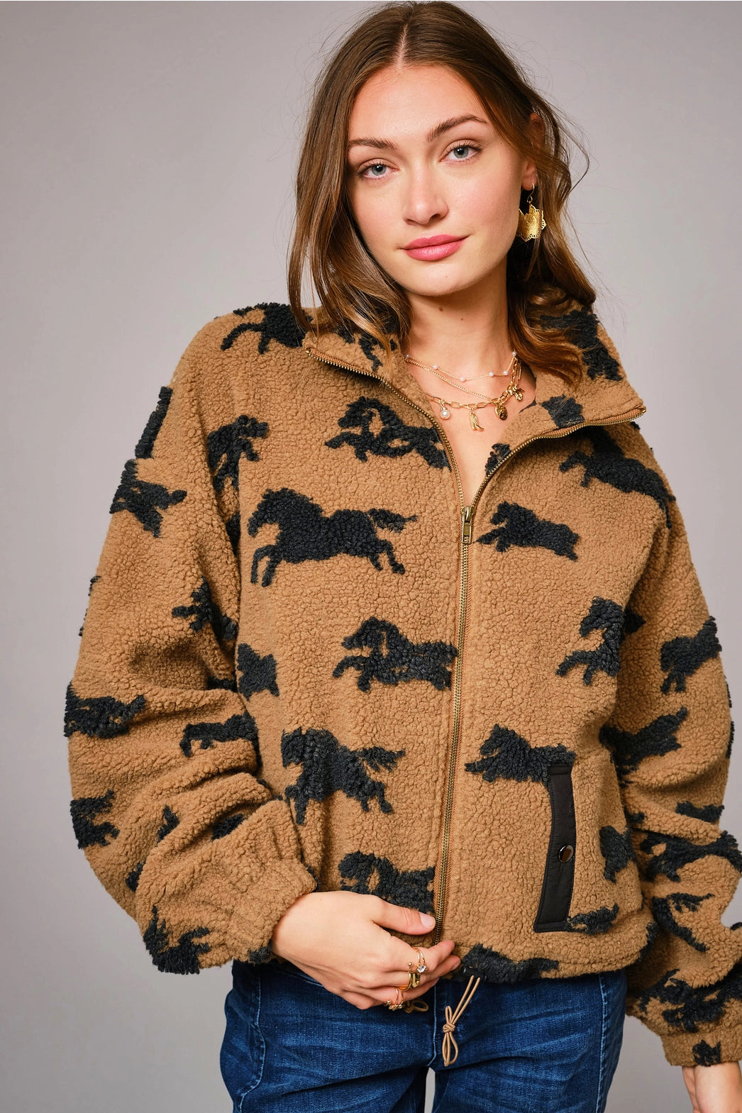 Woman wearing a brown fleece jacket with horse pattern against a gray background