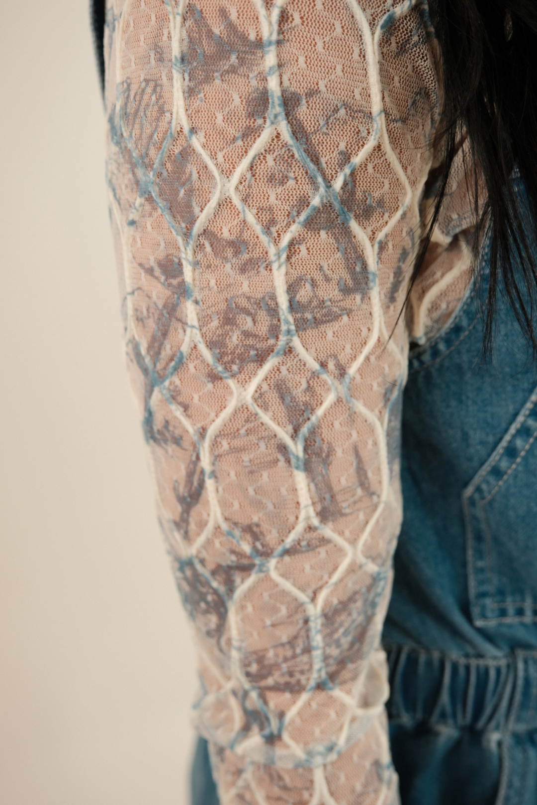 Close‑up of the mesh fabric showing embroidered cactus, horse and boot designs in contrasting color on sheer blue and cream top.