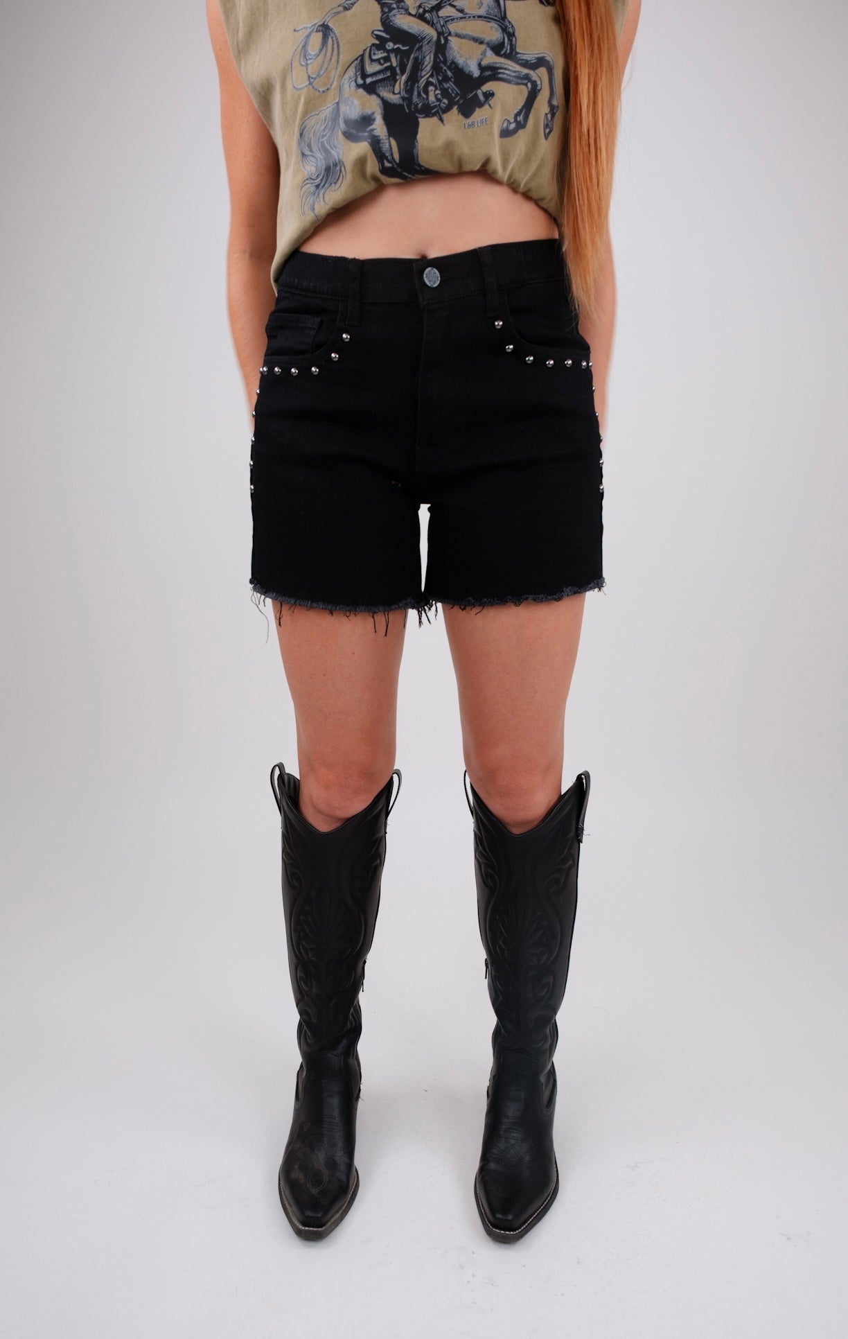 Person wearing black denim shorts with studded details and black knee-high boots on a white background