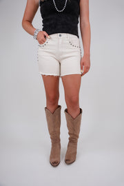 Person wearing white studded shorts and brown knee-high boots on a plain background