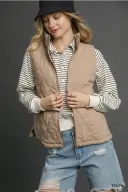 Woman wearing a beige vest over a striped shirt with ripped jeans.