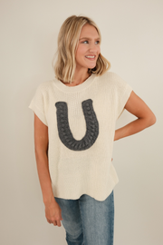 Chunky knit Wrangler’s Charm sweater in cream with ribbed sleeveless style and bold horseshoe motif to infuse cowgirl charm into any outfit.