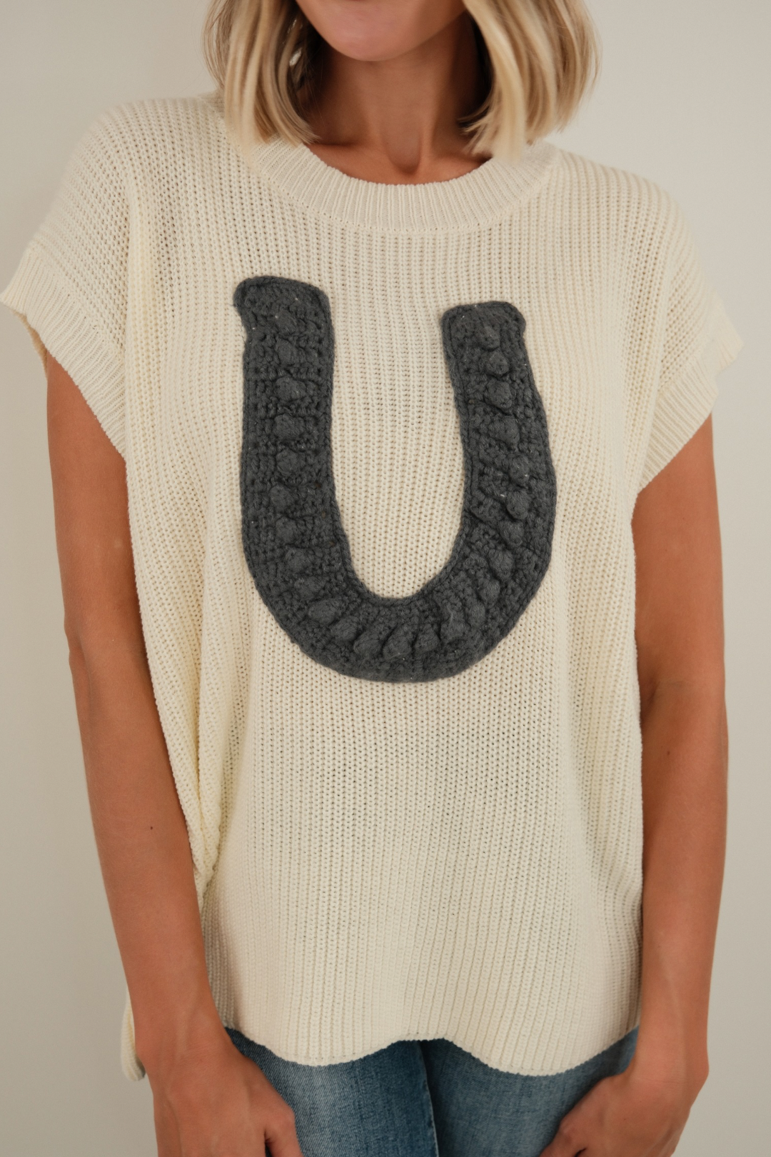 Front view of Wrangler’s Charm Sweater in cream, chunky ribbed sleeveless knit with bold horseshoe motif and western cowgirl style.