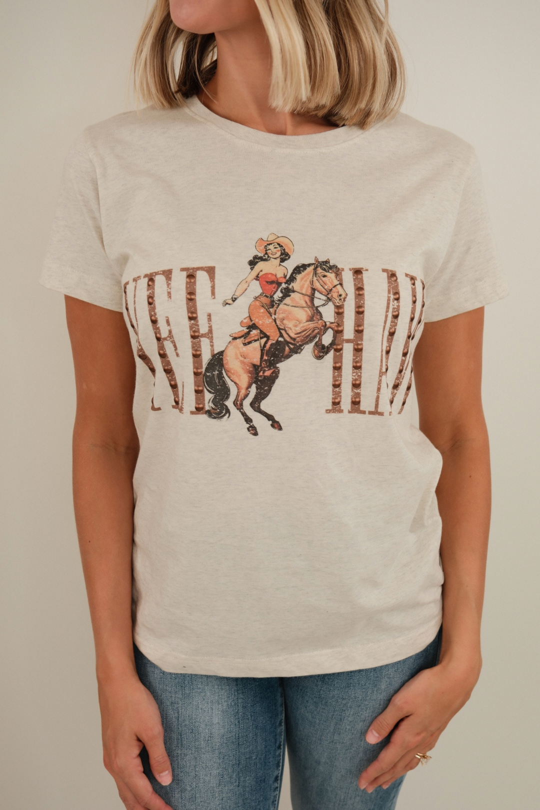 Close-up of Yeehaw Studded Tee highlighting cowgirl bronco graphic and bronze studded ‘Yeehaw’ detail.